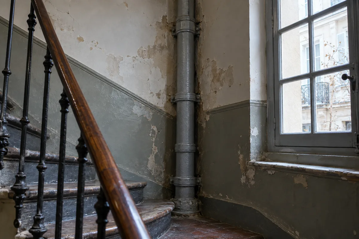 Colonne en fonte grise dans l&rsquo;angle d&rsquo;une cage d&rsquo;escalier d&rsquo;immeuble ancien